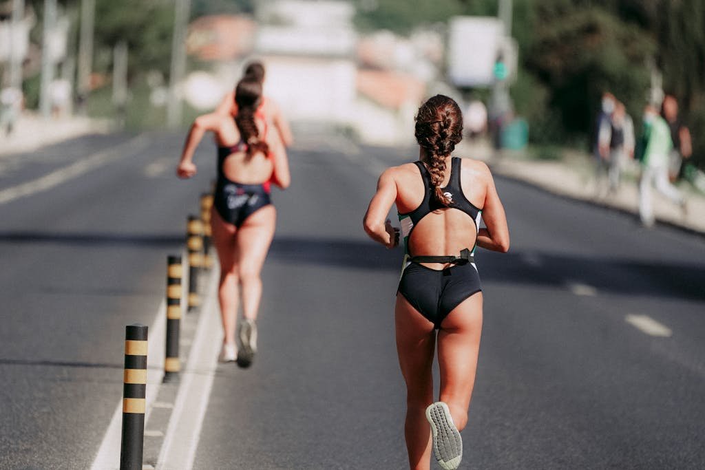 Two women athletes running on an open road during a marathon event, showcasing endurance and determination.